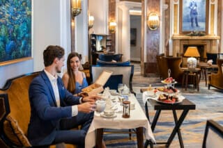 Paar genießt Tee und feine Leckereien in elegantem Hotelrestaurant mit stilvollem Ambiente.