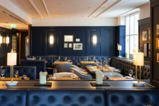 Elegantes Restaurant mit blauen Wänden, stilvollen Tischen und gemütlichen Sitzbereichen.