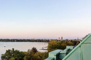 Blick über einen See mit Segelboot und Stadtansicht im Hintergrund bei Sonnenuntergang.