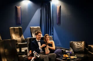 Couple in elegant clothes enjoying snacks in a modern cinema.