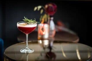 Eleganter Cocktail in einem Glas mit Rosmarin, auf einem Tisch in stilvollem Ambiente.