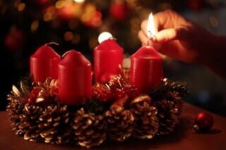 Rote Kerzen auf einem Adventskranz mit Tannenzweigen und Weihnachtsdekoration.
