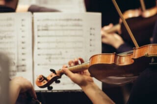 Violinenspieler mit Notenblättern im Hintergrund während eines Orchesterkonzerts.