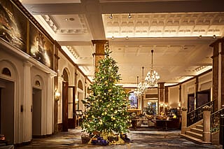 Festively decorated Christmas tree in the elegant hotel lobby with chandeliers.
