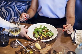 Frau genießt ein kunstvoll angerichtetes Gericht mit Gemüse und Wein im Restaurant.