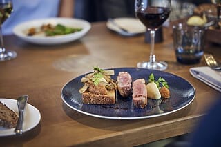 Gourmetgericht mit Fleisch, Gemüse, Püree und Rotwein in einem eleganten Restaurant.