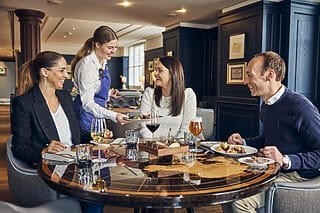 Freundliche Bedienung serviert Essen an Tisch mit vier Gästen in elegantem Restaurant.