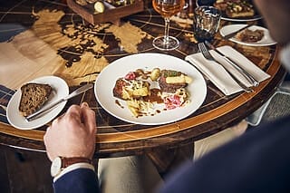 Gourmet-Gericht mit Fleisch, Kartoffeln und Gemüse auf einem stilvollen Tisch mit Weltkarte.