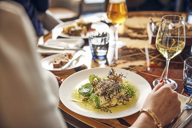 Gourmetgericht mit frischen Kräutern, serviert mit Weißwein und Brot auf einem stilvollen Tisch.