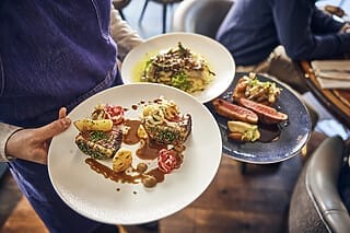 Kellner serviert zwei Teller mit feinem Fleisch, Beilagen und Saucen in einem Restaurant.