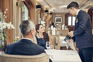 Elegantes Restaurant mit Gästen und Kellner, der Wein serviert. Stilvolle Atmosphäre und Dekor.