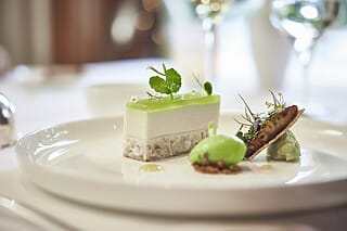 Dessert auf einem Teller: grüne Mousse, Sorbet und Keks, dekoriert mit frischen Kräutern.