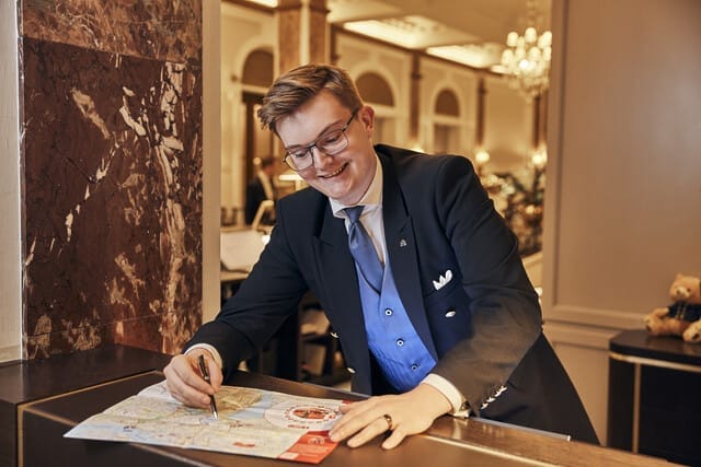 Hotelmitarbeiter zeichnet auf einer Karte, um Gästen hilfreiche Informationen zu bieten.