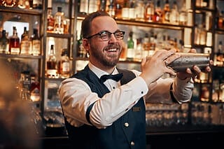 Barkeeper schüttelt einen Cocktail hinter einer gut gefüllten Bar mit Spirituosen.