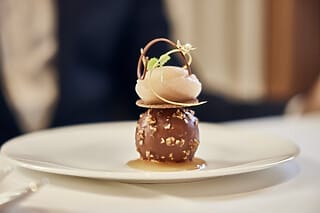 Dekadentes Dessert mit Schokoladenkugel, Sorbet und dekorativen Elementen auf einem Teller.