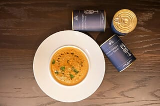 Hummersuppe in einer weißen Schüssel, mit Dosen im Hintergrund auf einem Holztablett.