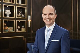 Hotel Atlantic Professioneller Mann in Anzug lächelt vor elegantem Hintergrund mit Regalen.