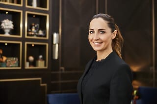 Hotel Atlantic Professionelle Frau in schwarzem Blazer lächelt vor elegantem Hintergrund mit Regalen.