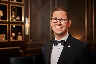 Lächelnder Mann im Anzug mit Fliege, vor elegantem Hintergrund in einem modernen Raum.