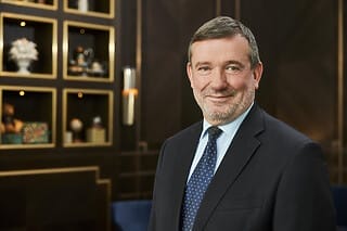 Porträt eines lächelnden Mannes in Anzug vor elegantem Hintergrund mit Regalen.