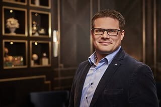 Professionelles Porträt eines Mannes in einem eleganten Raum mit Regal im Hintergrund.
