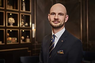 Professioneller Mann in Anzug mit buntem Einstecktuch vor elegantem Hintergrund.