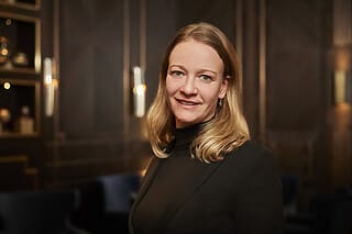 Professionelle Frau mit blonden Haaren in eleganter Umgebung, lächelnd und selbstbewusst.