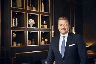 Hotel Atlantic Geschäftsmann in Anzug lächelt vor einer eleganten Wand mit dekorativen Regalen.