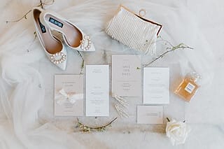 Elegante Brautschuhe, Einladungen und Accessoires auf einem marmorierten Tisch arrangiert.