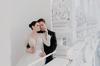 Brautpaar in eleganter Hochzeitskleidung posiert an einer weißen Balustrade.