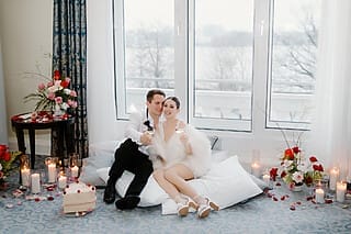 Paar mit Cocktails, umgeben von Blumen und Kerzen, in romantischer Hotelatmosphäre.