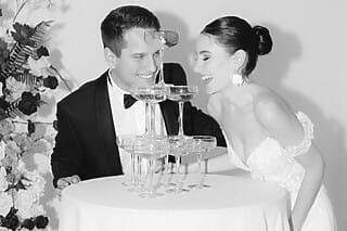 Brautpaar lächelt beim Anstoßen mit Sektgläsern auf einer eleganten Hochzeit.