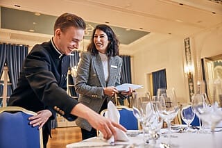Zwei Restaurantmitarbeiter bereiten einen elegant gedeckten Tisch für eine Veranstaltung vor.