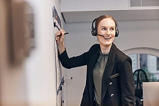 Frau mit Headset schreibt an einer Wandtafel in einem modernen Büro.