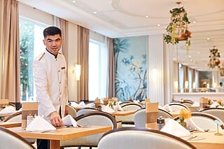 Kellner in eleganter Uniform deckt einen Tisch in einem stilvollen Restaurant.