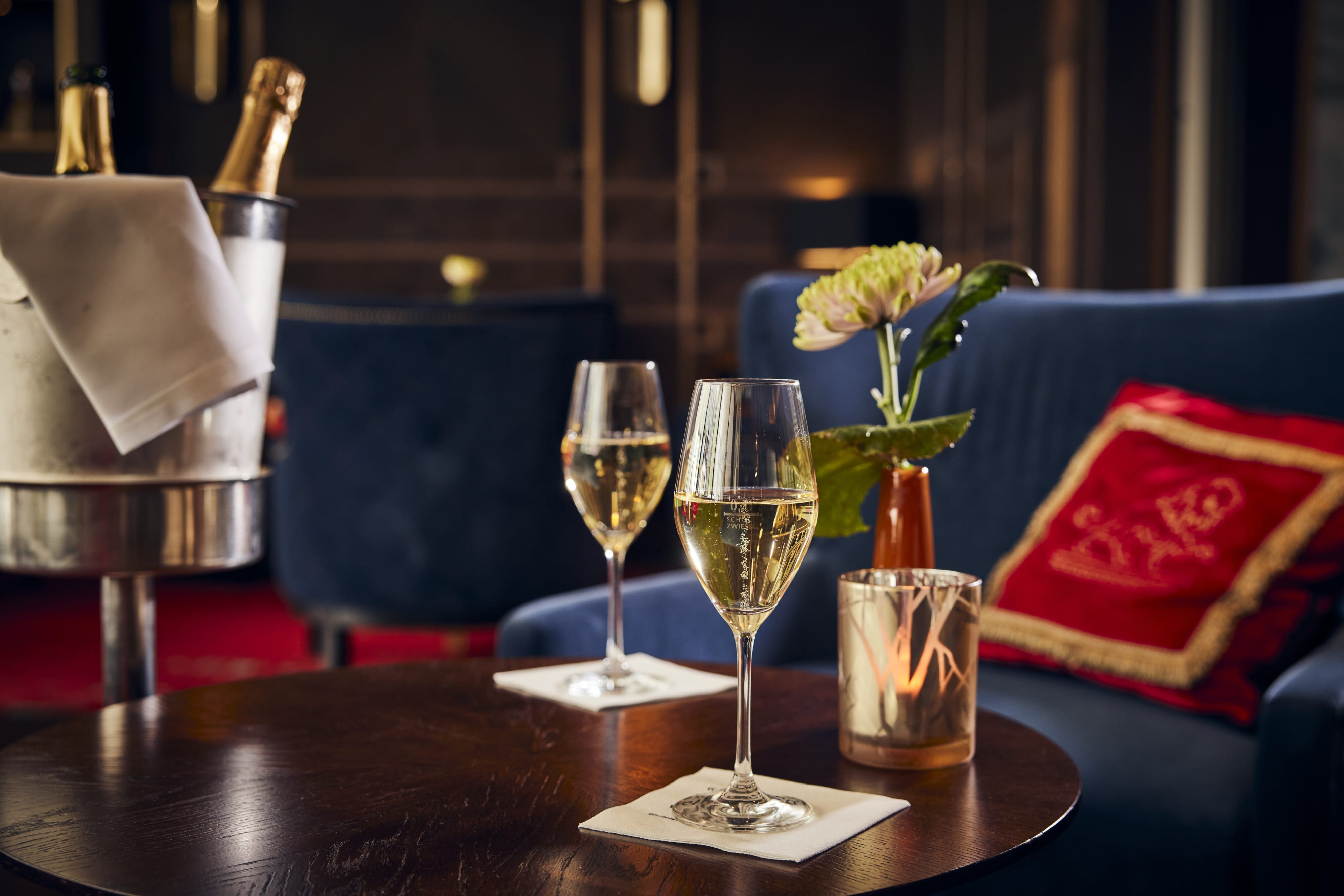 Hotel Atlantic Zwei Gläser Sekt auf einem Tisch neben einer Blume und einem Champagner-Eisbehälter.