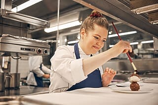 Köchin verziert ein Dessert kreativ in einer modernen Restaurantküche.