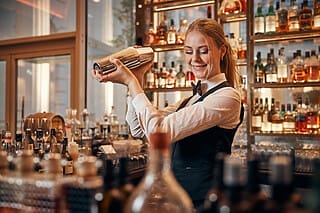 Bartender schüttelt Cocktails in einer stilvollen Bar mit einer Vielzahl von Spirituosen im Hintergrund.