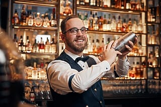 Bartender schüttelt Cocktails vor einer gut bestückten Bar mit Spirituosen.