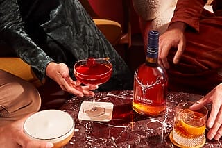 Cocktails und Dalmore Whisky auf einem marmorierten Tisch, umgeben von stilvollen Gästen.