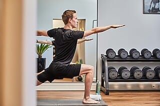 Hotel Atlantic Mann in Sportkleidung übt Yoga in modernem Fitnessraum mit Gewichten im Hintergrund.