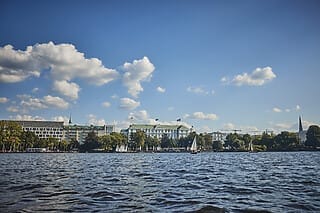 Panorama von Hamburgs Binnenalster mit Segelbooten und klarblauem Himmel.