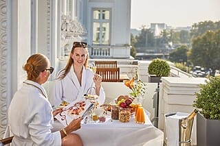 Hotel Atlantic Zwei Frauen in Bademänteln genießen ein luxuriöses Frühstück auf einer sonnigen Terrasse.