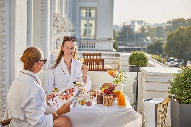 Zwei Frauen in Bademänteln genießen ein luxuriöses Frühstück auf einer sonnigen Terrasse.