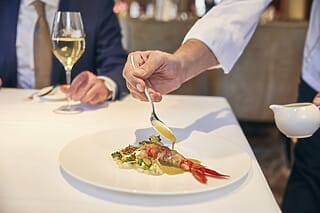 Ein Kellner serviert ein Gourmetgericht mit Garnelen und Sauce in einem eleganten Restaurant.