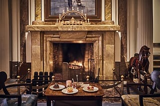 Cosy fireplace lounge with cake and a warm fire, surrounded by elegant decorations.