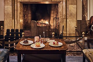 Gemütliche Teestunde vor dem Kamin mit köstlichen Desserts und stilvollen Sesseln.
