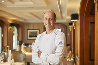 Koch im Restaurant des Hotel Atlantic Hamburg, lächelnd mit verschränkten Armen.
