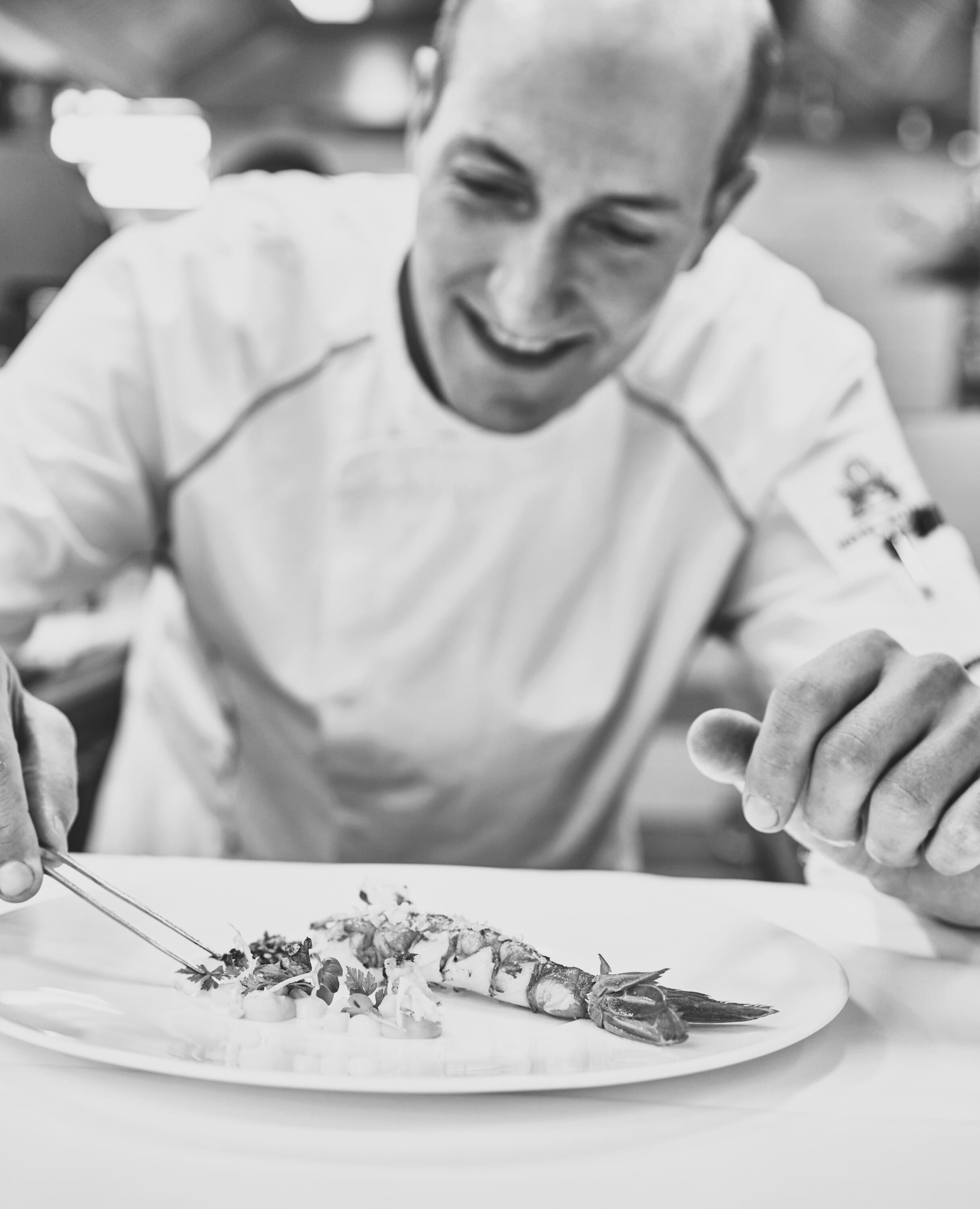 Hotel Atlantic Koch präsentiert kunstvoll angerichtetes Gericht mit Meeresfrüchten auf weißem Teller.