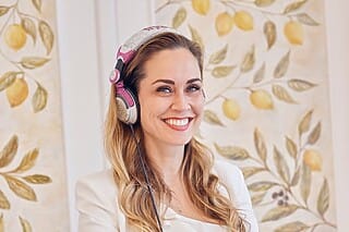 Lächelnde Frau mit Kopfhörern vor einer dekorativen Wand mit Zitronenmotiven.